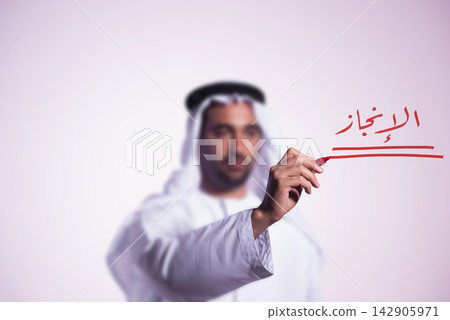 Arab businessman in traditional kandura writing 'achievement' in Arabic with red marker to convey success and goals Arab businessman in traditional kandura writing 'achievement' in Arabic with red marker to convey success and goals 142905971