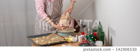 A man is getting ready for pre-Christmas dinner by baking chicken with potatoes. He arranges food on a tray while festive decorations are nearby in the kitchen, banner A man is getting ready for pre-Christmas dinner by baking chicken with potatoes. He arranges food on a tray while festive decorations are nearby in the kitchen, banner 142906530