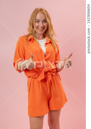 Cheerful blonde woman smiling at the camera, showing a positive gesture with both hands on a pink background, expressing success and satisfaction Cheerful blonde woman smiling at the camera, showing a positive gesture with both hands on a pink background, expressing success and satisfaction 142906604