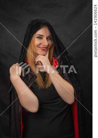 Young adult woman with red lipstick and green eyes, smiling while posing in a mysterious costume, representing concepts of secrecy, magic, and Halloween Young adult woman with red lipstick and green eyes, smiling while posing in a mysterious costume, representing concepts of secrecy, magic, and Halloween 142906624
