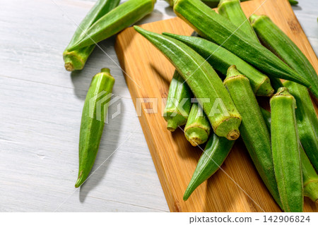 Fresh okra arranged on a wooden cutting board 142906824