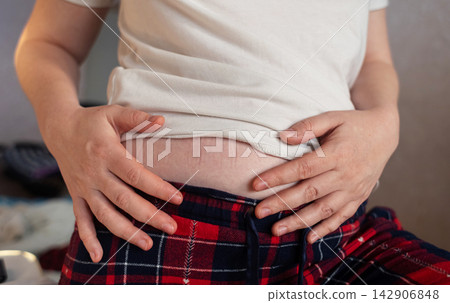 Close-up of a woman touching elastic waistband marks on her stomach skin. Tight clothing imprint caused by uncomfortable waistband and skin pressure. Close-up of a woman touching elastic waistband marks on her stomach skin. Tight clothing imprint caused by uncomfortable waistband and skin pressure. 142906848