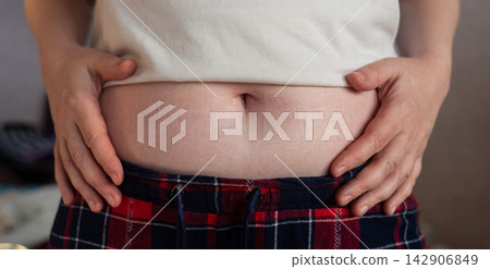 Close-up of a woman touching elastic waistband marks on her stomach skin. Tight clothing imprint caused by uncomfortable waistband and skin pressure. Close-up of a woman touching elastic waistband marks on her stomach skin. Tight clothing imprint caused by uncomfortable waistband and skin pressure. 142906849