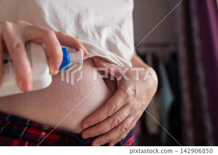 Woman applying moisturizing lotion dispenser cream on stretch marks on belly skin. Close up of female hands caring for stomach body skin. Woman applying moisturizing lotion dispenser cream on stretch marks on belly skin. Close up of female hands caring for stomach body skin. 142906850