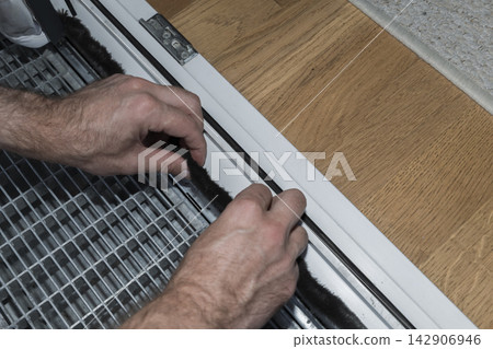 Person installing self adhesive brush seal on a window frame, illustrating effective door and window sealing for energy efficiency Person installing self adhesive brush seal on a window frame, illustrating effective door and window sealing for energy efficiency 142906946