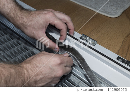 Person removing the protective layer from a self adhesive brush seal, illustrating effective door sealing for energy efficiency. Person removing the protective layer from a self adhesive brush seal, illustrating effective door sealing for energy efficiency. 142906953