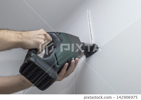 Person cleaning a wall ventilation unit with a handheld vacuum, illustrating seasonal home vent inspection and maintenance. 142906975