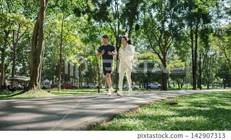 Asian couple jogging along park path for outdoor fitness and healthy lifestyle Asian couple jogging along park path for outdoor fitness and healthy lifestyle 142907313