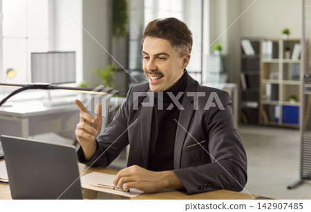 Businessman talking on laptop during online video call in bright modern office Businessman talking on laptop during online video call in bright modern office 142907485