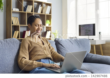 Smiling woman using laptop on sofa at home, remote work and online learning Smiling woman using laptop on sofa at home, remote work and online learning 142907486