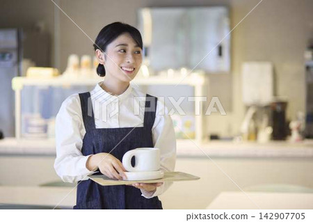 A female staff member carrying coffee on a tray at a cafe. A female staff member carrying coffee on a tray at a cafe. 142907705
