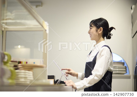 A female staff member enters an order into a POS terminal at a cafe. A female staff member enters an order into a POS terminal at a cafe. 142907730
