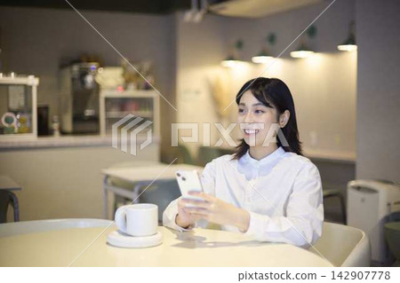 A woman smiles while using her smartphone in a cafe. A woman smiles while using her smartphone in a cafe. 142907778