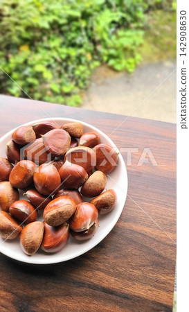Autumn delicacies: Freshly picked chestnuts served on a plate against a green background. Autumn delicacies: Freshly picked chestnuts served on a plate against a green background. 142908630