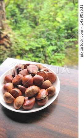 秋季美食:新鮮採摘的栗子盛放在盤子裡,以綠色為背景。 秋季美食:新鮮採摘的栗子盛放在盤子裡,以綠色為背景。 142908631