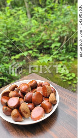 秋季美食:新鮮採摘的栗子盛放在盤子裡,以綠色為背景。 秋季美食:新鮮採摘的栗子盛放在盤子裡,以綠色為背景。 142908636