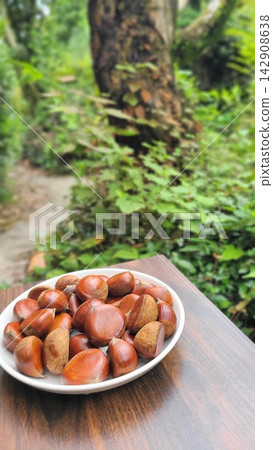 秋季美食:新鮮採摘的栗子盛放在盤子裡,以綠色為背景。 秋季美食:新鮮採摘的栗子盛放在盤子裡,以綠色為背景。 142908638