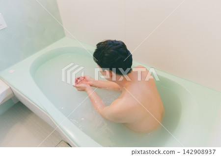 一名男子在浴缸裡泡澡，用手舀水。 142908937