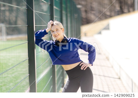 Young sportswoman relaxing after training on sports field Young sportswoman relaxing after training on sports field 142909025