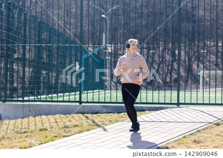 Young sporty woman running and listening to music with wireless headphones in the park Young sporty woman running and listening to music with wireless headphones in the park 142909046