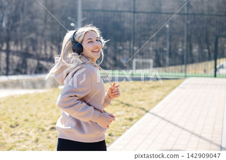 Young sportswoman running in the park listening music with headphones Young sportswoman running in the park listening music with headphones 142909047