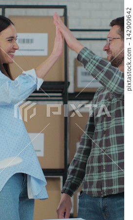 Vertical video. Happy man and woman high five each other. Business owners work in a warehouse. Computer usage, retail inventory checking, shipment preparation. Vertical video. Happy man and woman high five each other. Business owners work in a warehouse. Computer usage, retail inventory checking, shipment preparation. 142909642
