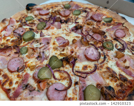 A savory artisan pizza topped with sliced sausage, pickles, red onion, and melted cheese inside a cardboard delivery box, capturing a rustic meal perfect for casual dining occasions A savory artisan pizza topped with sliced sausage, pickles, red onion, and melted cheese inside a cardboard delivery box, capturing a rustic meal perfect for casual dining occasions 142910323