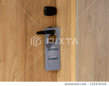 A do not disturb sign hanging on a wooden hotel room door handle, conveying a message of privacy, quiet, and guest comfort during a stay at a modern travel lodging establishment A do not disturb sign hanging on a wooden hotel room door handle, conveying a message of privacy, quiet, and guest comfort during a stay at a modern travel lodging establishment 142910326