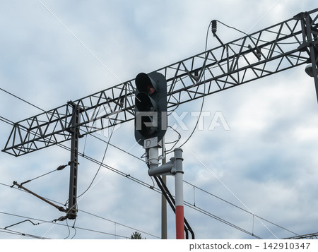 A railway signal light mounted on a steel gantry under a cloudy sky, controlling train movement and ensuring safety in a modern industrial transport infrastructure travel network system A railway signal light mounted on a steel gantry under a cloudy sky, controlling train movement and ensuring safety in a modern industrial transport infrastructure travel network system 142910347
