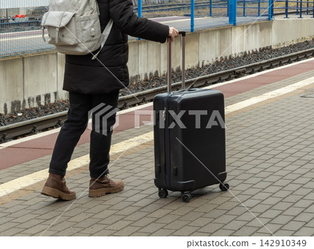 A traveler holding a rolling suitcase while standing on a platform, conveying the concept of transit and adventure during a journey at a modern train station in a bright day setting A traveler holding a rolling suitcase while standing on a platform, conveying the concept of transit and adventure during a journey at a modern train station in a bright day setting 142910349