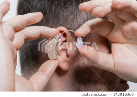 A man holds a small medical hearing aid device near an ear, illustrating the practical process of inserting an accessory to assist with sensory impairment and improved sound quality 142910366