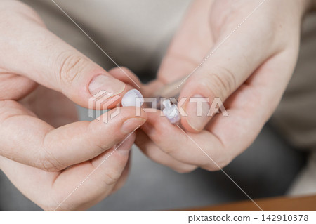 A person replaces a silicone ear tip on a small hearing aid device, demonstrating routine maintenance and care for assistive medical technology to improve sound quality for the user A person replaces a silicone ear tip on a small hearing aid device, demonstrating routine maintenance and care for assistive medical technology to improve sound quality for the user 142910378