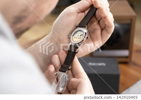 A man examines an automatic mechanical watch with a transparent case back, displaying intricate internal components while highlighting luxury craftsmanship in a professional retail shop A man examines an automatic mechanical watch with a transparent case back, displaying intricate internal components while highlighting luxury craftsmanship in a professional retail shop 142910405