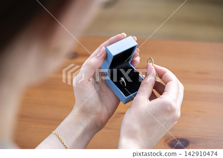 A woman holds a small light blue jewelry box displaying delicate gold diamond hoop earrings, highlighting luxury gift giving and elegant fashion accessories for special occasions A woman holds a small light blue jewelry box displaying delicate gold diamond hoop earrings, highlighting luxury gift giving and elegant fashion accessories for special occasions 142910474