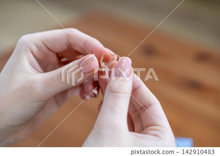 A woman holds a small gold hoop earring between her fingers with well manicured nails, showcasing a delicate piece of jewelry for fashion styling or retail advertisement presentation 142910483