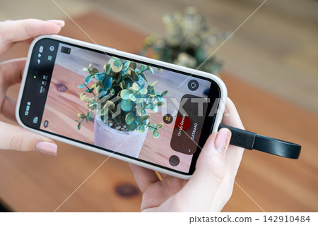 Person using a smartphone connected to an external ssd for recording footage of a plant, illustrating modern mobile photography storage solutions and high quality digital video capture 142910484
