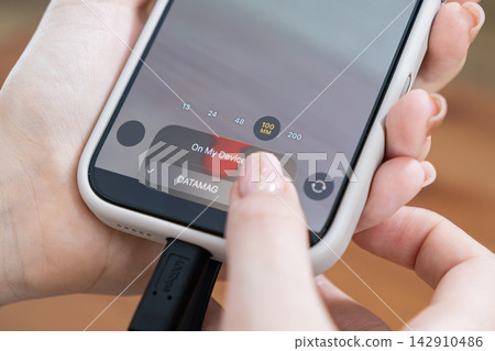 A person connecting an external SSD to a smartphone to manage files, using mobile technology for efficient data storage and digital content transfer in a modern workspace environment A person connecting an external SSD to a smartphone to manage files, using mobile technology for efficient data storage and digital content transfer in a modern workspace environment 142910486