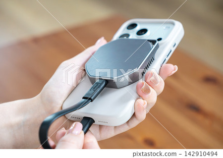 Person holding a smartphone with an attached portable ssd for external storage, showcasing modern mobile technology, data management, and digital workflow efficiency in a workspace 142910494
