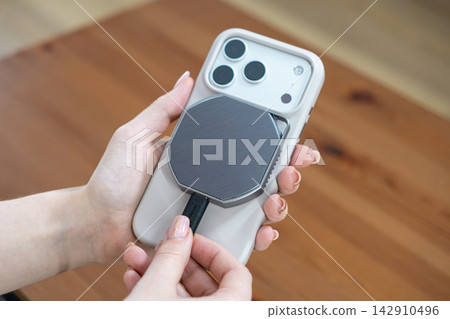 A hand plugging a cable into an external magnetic SSD attached to a modern smartphone, representing portable data storage, fast file transfer, and mobile backup solutions for creators A hand plugging a cable into an external magnetic SSD attached to a modern smartphone, representing portable data storage, fast file transfer, and mobile backup solutions for creators 142910496