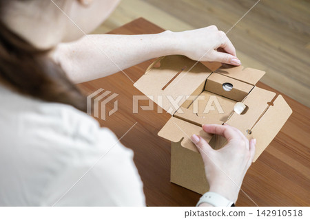 Person opening a small brown cardboard box on a wooden desk, reflecting the sustainable e-commerce unboxing experience of a new product delivery within a home or professional setting Person opening a small brown cardboard box on a wooden desk, reflecting the sustainable e-commerce unboxing experience of a new product delivery within a home or professional setting 142910518