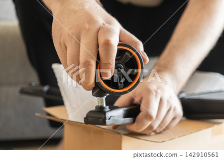 A person installs a replacement caster wheel onto a metal office chair leg while unpacking a delivery, illustrating the assembly process for furniture maintenance in a home setting A person installs a replacement caster wheel onto a metal office chair leg while unpacking a delivery, illustrating the assembly process for furniture maintenance in a home setting 142910561