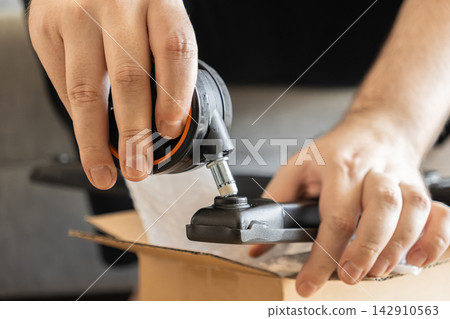 A person assembling a black office chair by inserting the rolling castor wheel into the metal base, representing a home furniture DIY project task during the interior setup process A person assembling a black office chair by inserting the rolling castor wheel into the metal base, representing a home furniture DIY project task during the interior setup process 142910563