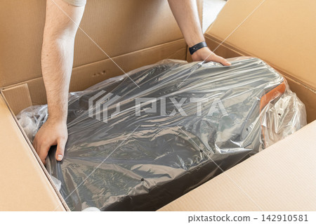 Person unpacking a new gaming chair from a large cardboard box, representing home delivery, online shopping, furniture assembly, and the excitement of setting up a workspace indoors 142910581