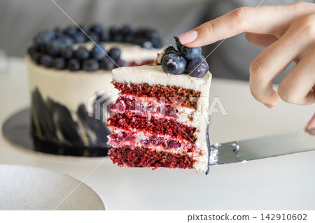 A person lifts a slice of gourmet red velvet berry cake with a silver server from a whole dessert, highlighting culinary craft and indulgence in a bright modern kitchen restaurant A person lifts a slice of gourmet red velvet berry cake with a silver server from a whole dessert, highlighting culinary craft and indulgence in a bright modern kitchen restaurant 142910602