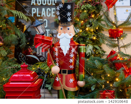 A festive soldier nutcracker statue stands beside a bright red mailbox and pine tree, conveying a joyful holiday atmosphere in a decorated urban shop window during the winter season A festive soldier nutcracker statue stands beside a bright red mailbox and pine tree, conveying a joyful holiday atmosphere in a decorated urban shop window during the winter season 142910648