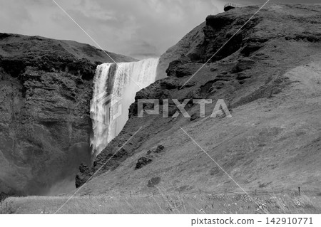 Black and white Skogafoss waterfall with grassy slopes in southern Iceland Black and white Skogafoss waterfall with grassy slopes in southern Iceland 142910771