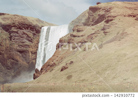 Skogafoss waterfall and steep grassy cliffs in a muted summer Iceland landscape Skogafoss waterfall and steep grassy cliffs in a muted summer Iceland landscape 142910772
