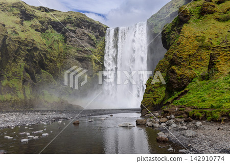 Skogafoss waterfall at Skogar, Iceland, above a rocky river foreground with green mossy cliffs Skogafoss waterfall at Skogar, Iceland, above a rocky river foreground with green mossy cliffs 142910774
