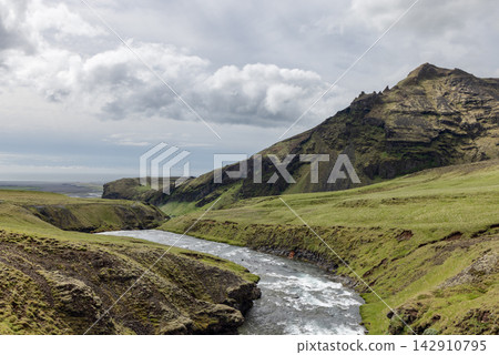 Skoga River Curving Below a Rugged Mountain and Green Slopes in Cloudy Iceland Skoga River Curving Below a Rugged Mountain and Green Slopes in Cloudy Iceland 142910795