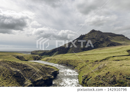 Skoga River Rapids Below a Rugged Mountain and Cloudy Sky in Green Iceland Skoga River Rapids Below a Rugged Mountain and Cloudy Sky in Green Iceland 142910796